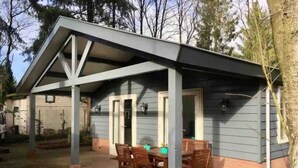 Eine überdachte Terrasse mit Tisch und Stühlen, eine kleine Veranda und ein Fenster.