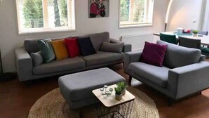 Ein Wohnzimmer mit einer grauen Sofagarnitur, einem runden Couchtisch mit einer Pflanze und Kunstwerken an den Wänden.