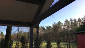 Ein überdachter Außenbereich mit Blick auf ein Wiesfeld und Bäume.