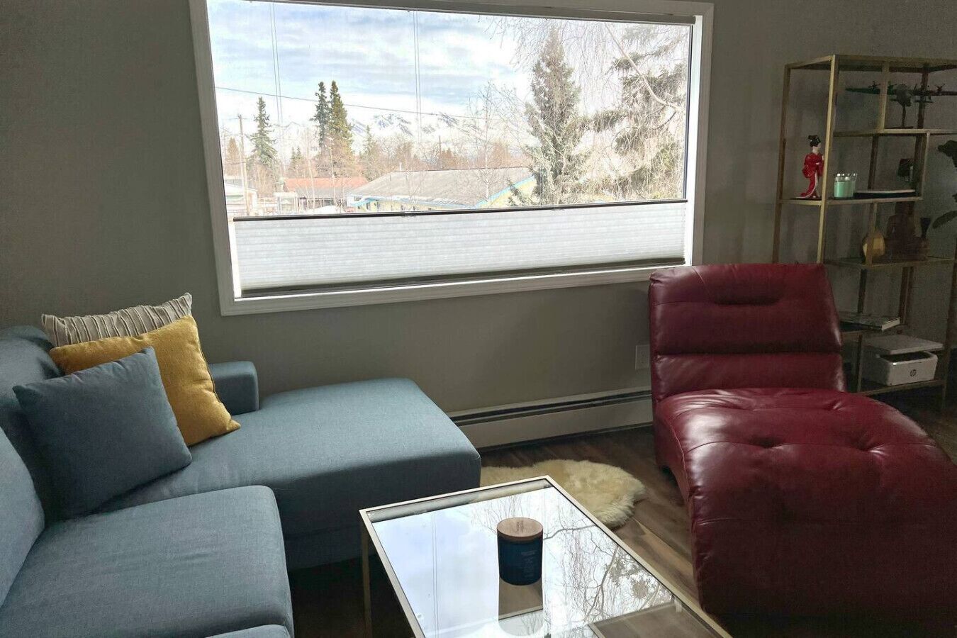 Ein Wohnzimmer mit grauem Sofa, einem roten Sessel, einem Glastisch und einem Bücherregal.