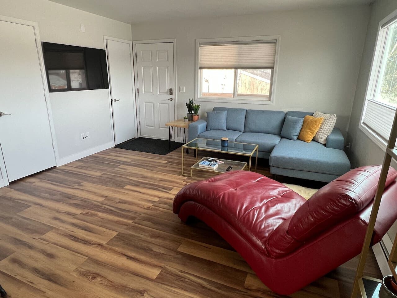 A spacious living area with a blue sofa, a red leather chair, and a glass coffee table.