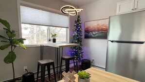 A modern kitchen with a wooden table, two bar stools, a Christmas tree, and a refrigerator. - Contemporary 2 Bedrooms Super location (Anchorage)