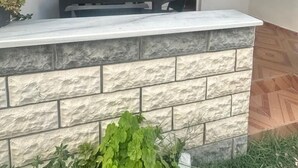 Een overdekt terras met een stenen muur, een barbecue en een raam met uitzicht op het interieur.