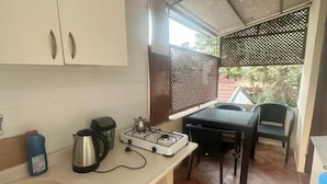 Een compacte keuken met een gasfornuis, waterkoker en spoelbak. Er is een tafel met stoelen in het aangrenzende eetgedeelte.