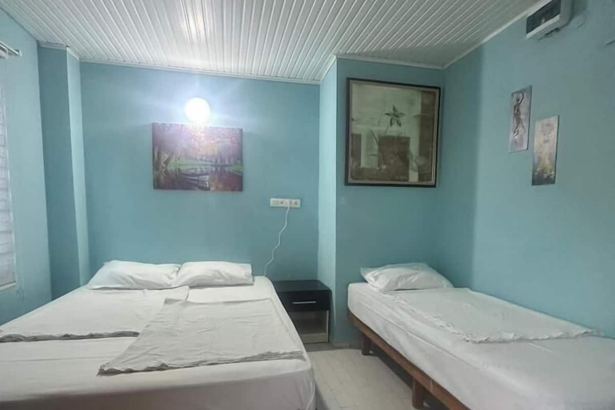 A room with two beds, a nightstand, a wall-mounted light, and a framed picture.