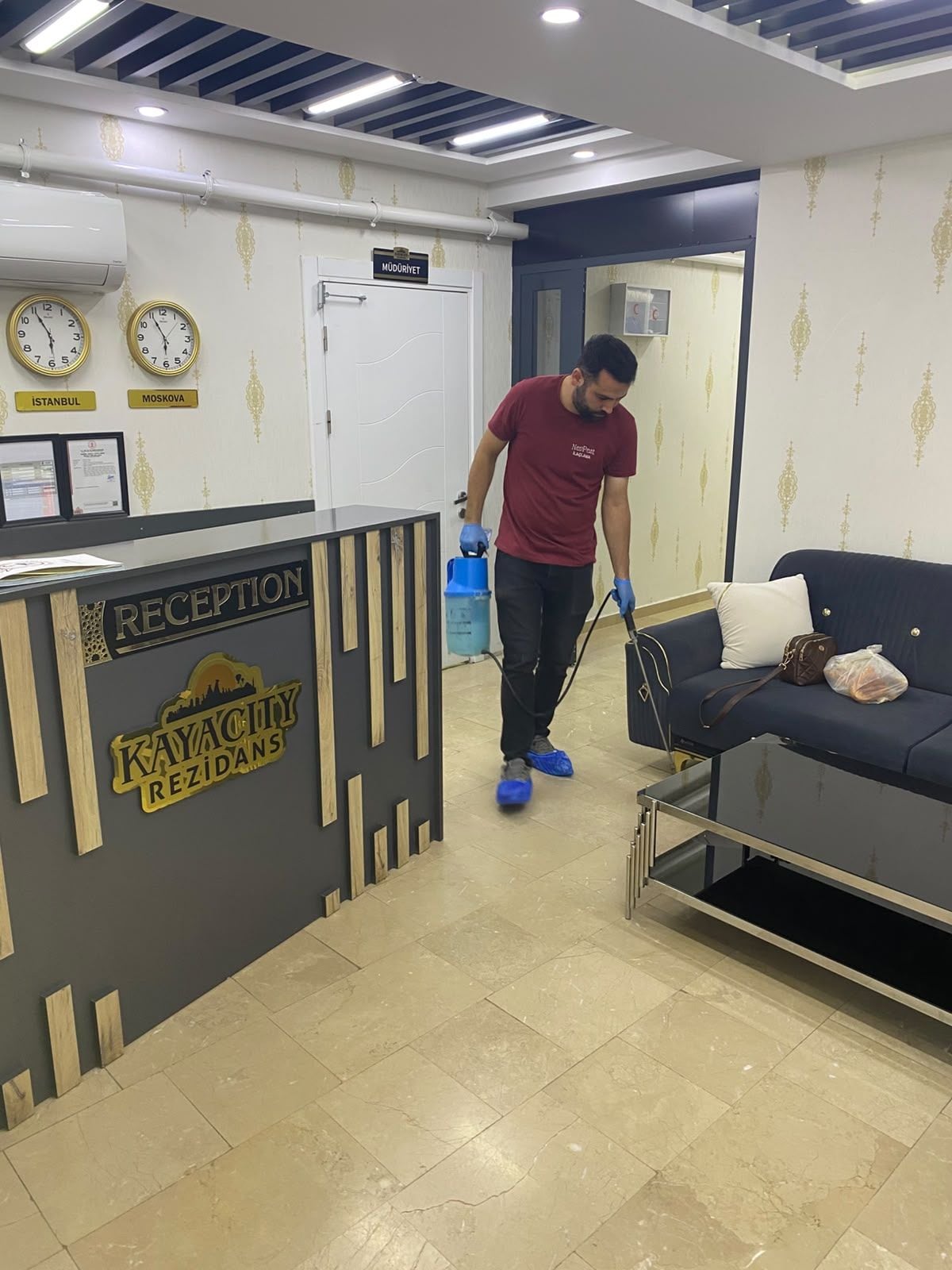 A reception area with a reception desk, clocks, and a person cleaning the floor.