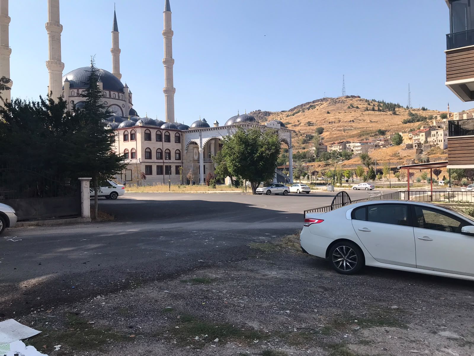 Une mosquée dotée de plusieurs minarets et d’un dôme, entourée de bâtiments résidentiels et d’un paysage vallonné.