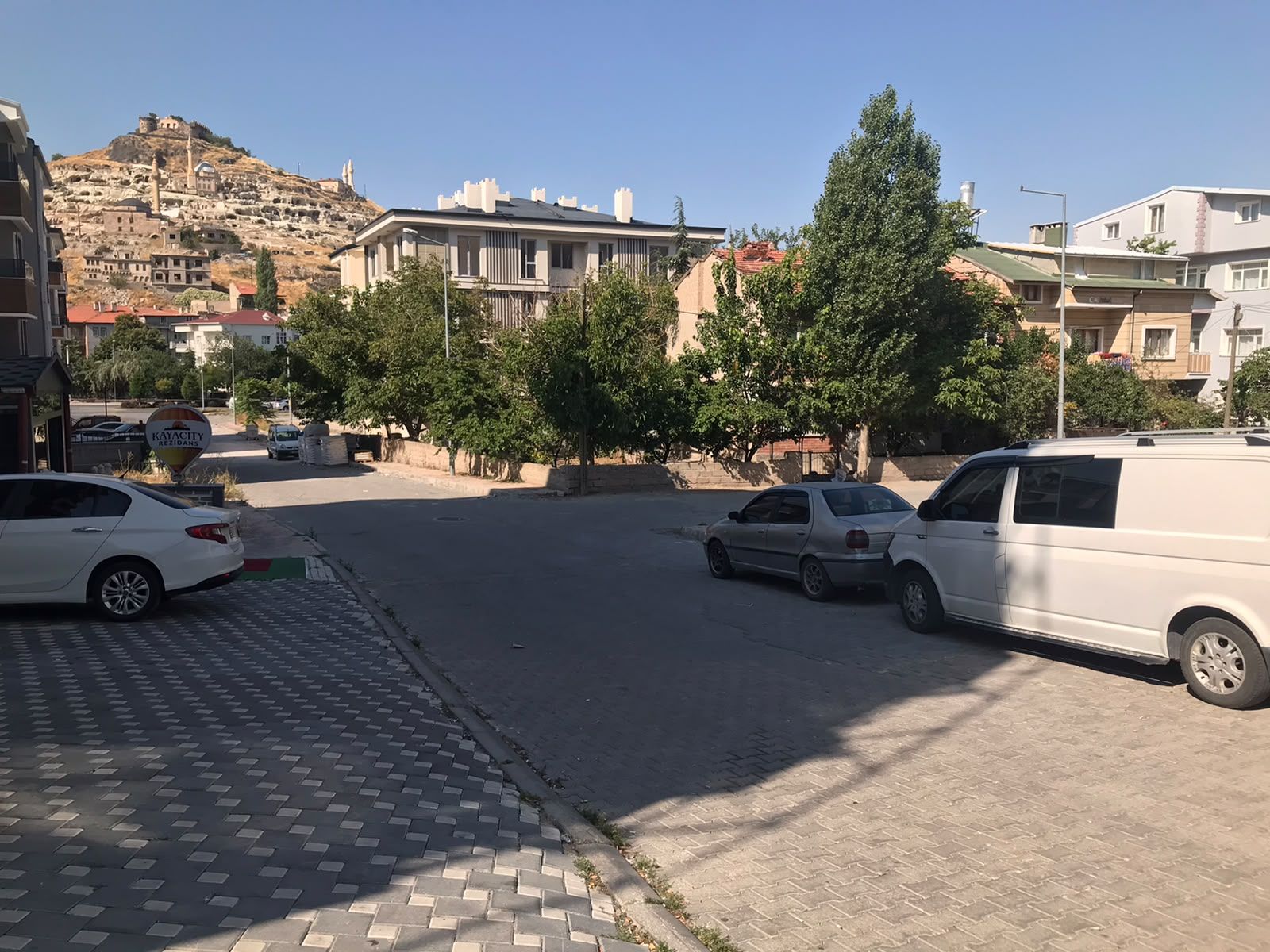 A street with parked cars, a sign for 'KAYACITY REZIDANS,' and buildings in the background.
