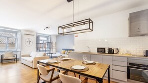 A modern kitchen with a wooden dining table, white cabinets, and a built-in oven. - Colosseum Building - Apartment Gamma (Lisbon)