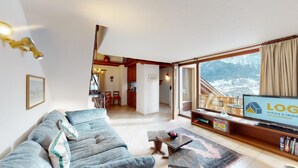 Ein Wohnzimmer mit einer Couch, einem Couchtisch, einem Fernseher und Blick auf einen verschneiten Berg.