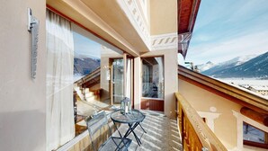 Ein Balkon mit Tisch und Stühlen, Blick auf schneebedeckte Berge und einem Holgitter.