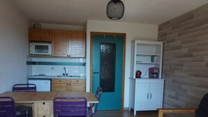A compact kitchen with wooden cabinets, a microwave, and a teal-framed door. - Cozy apartment in Autrans center, 4 pers, south terrace, pets allowed (Autrans-Méaudre en Vercors-Autrans)