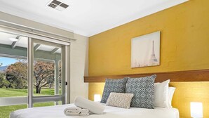 A bedroom with a bed, a nightstand, a painting, and a view of a tree and grass. - Martha's Homestead - A relaxing Lovedale getaway (Lovedale)