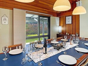 A dining room with a large table set for a meal, a bottle of wine, and a view of the outdoors.