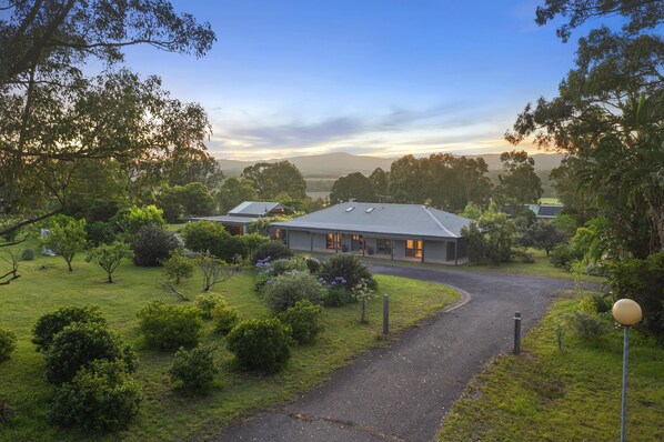 A building with a paved driveway, surrounded by greenery and trees.