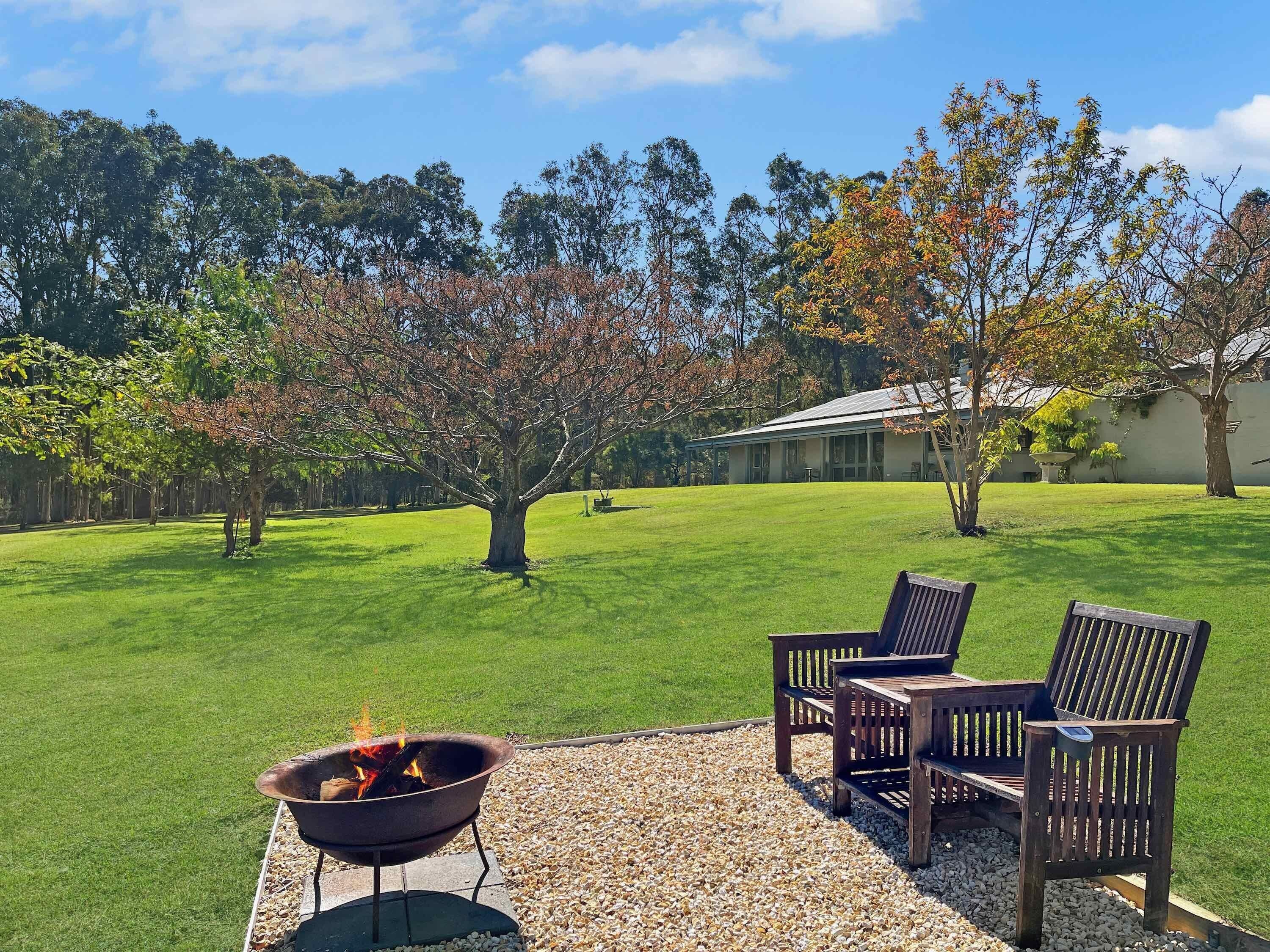 A backyard with a fire pit, two wooden chairs, and a lawn.
