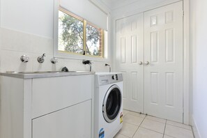 Un lavadero con lavadora de carga frontal, una ventana sobre el lavabo y una puerta blanca.