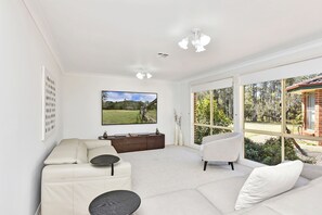 A modern living room with a large TV, comfortable seating, and a view of the outdoors.