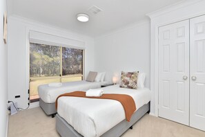 Un dormitorio con dos camas, una ventana con vistas a árboles, una puerta y un accesorio de iluminación en el techo.