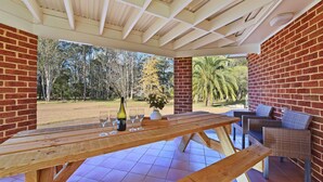 An outdoor patio with a wooden table, chairs, and a bottle of wine. - Home Among the Gum Trees - Lovedale (Lovedale)
