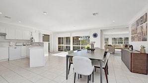 A modern kitchen with white cabinetry, a dining area with a large table, and a living space with a sofa and a coffee table. - Home Among the Gum Trees - Lovedale (Lovedale)