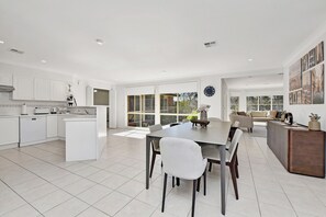 Una cocina moderna con armarios blancos, un comedor con una mesa grande y una sala de estar con un sofá y una mesa de centro.