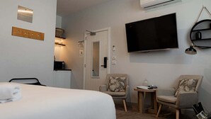 Ett hotellrum med en säng, två fåtöljer, ett litet bord, en tv och en vägghylla.
