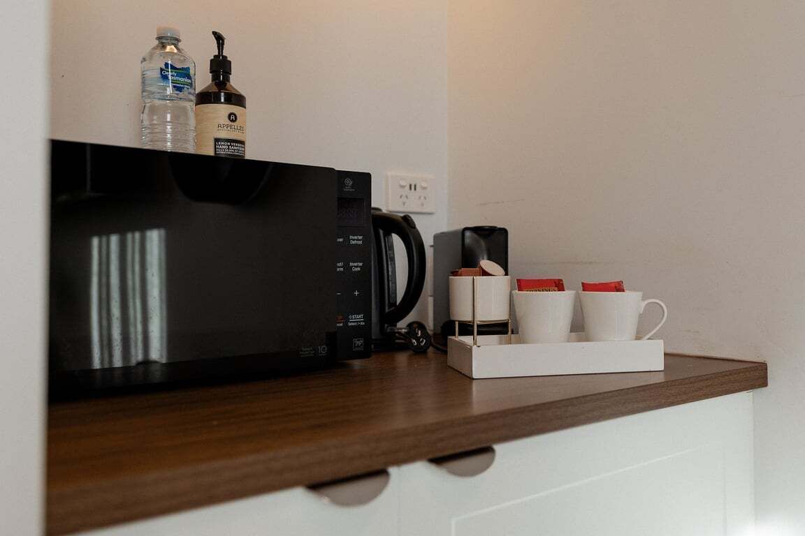 A kitchen area with a microwave, coffee maker, and a coffee station with cups and a box.