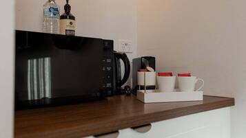 A kitchen area with a microwave, coffee maker, and a coffee station with cups and a box.