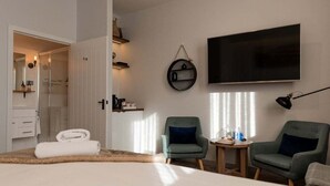 Ett hotellrum med en säng, två fåtöljer, ett litet bord, en tv och en spegel.