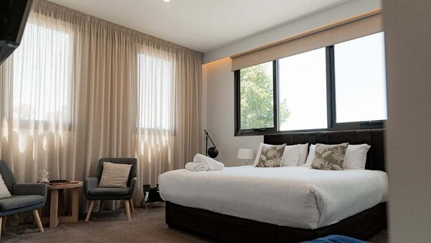 Una camera d'albergo con un letto grande, due poltrone, un tavolino e una finestra con tende.