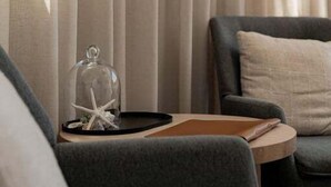 Una stanza con un divano grigio scuro, un tavolino in legno e una cupola di vetro decorata con una stella marina.