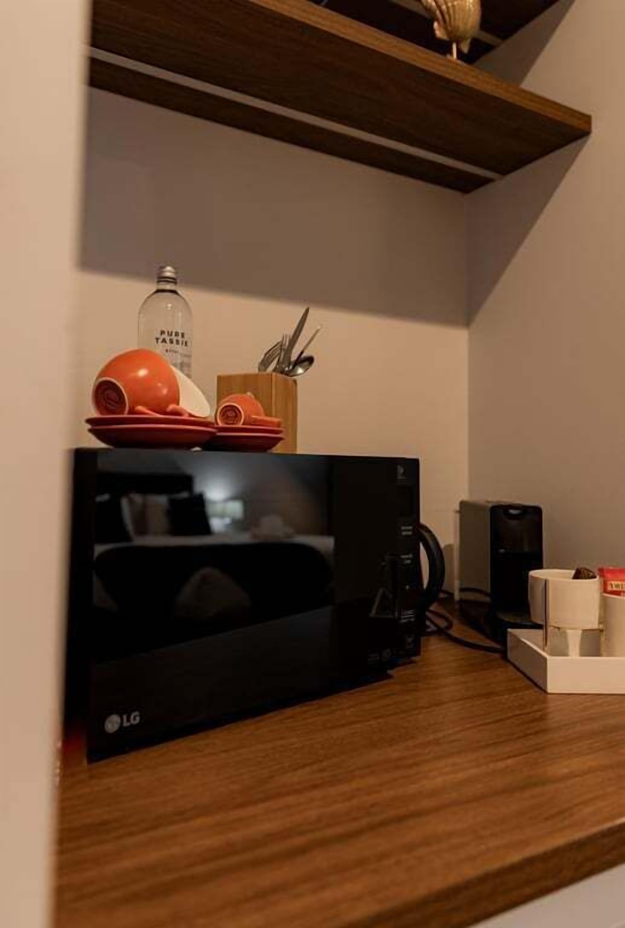 Une cuisine équipée d’un four à micro-ondes LG, d’une machine à café et d’une étagère contenant de la vaisselle et des ustensiles.