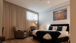 Habitación de hotel con una cama grande, dos sillones, un escritorio y un cuadro en la pared.