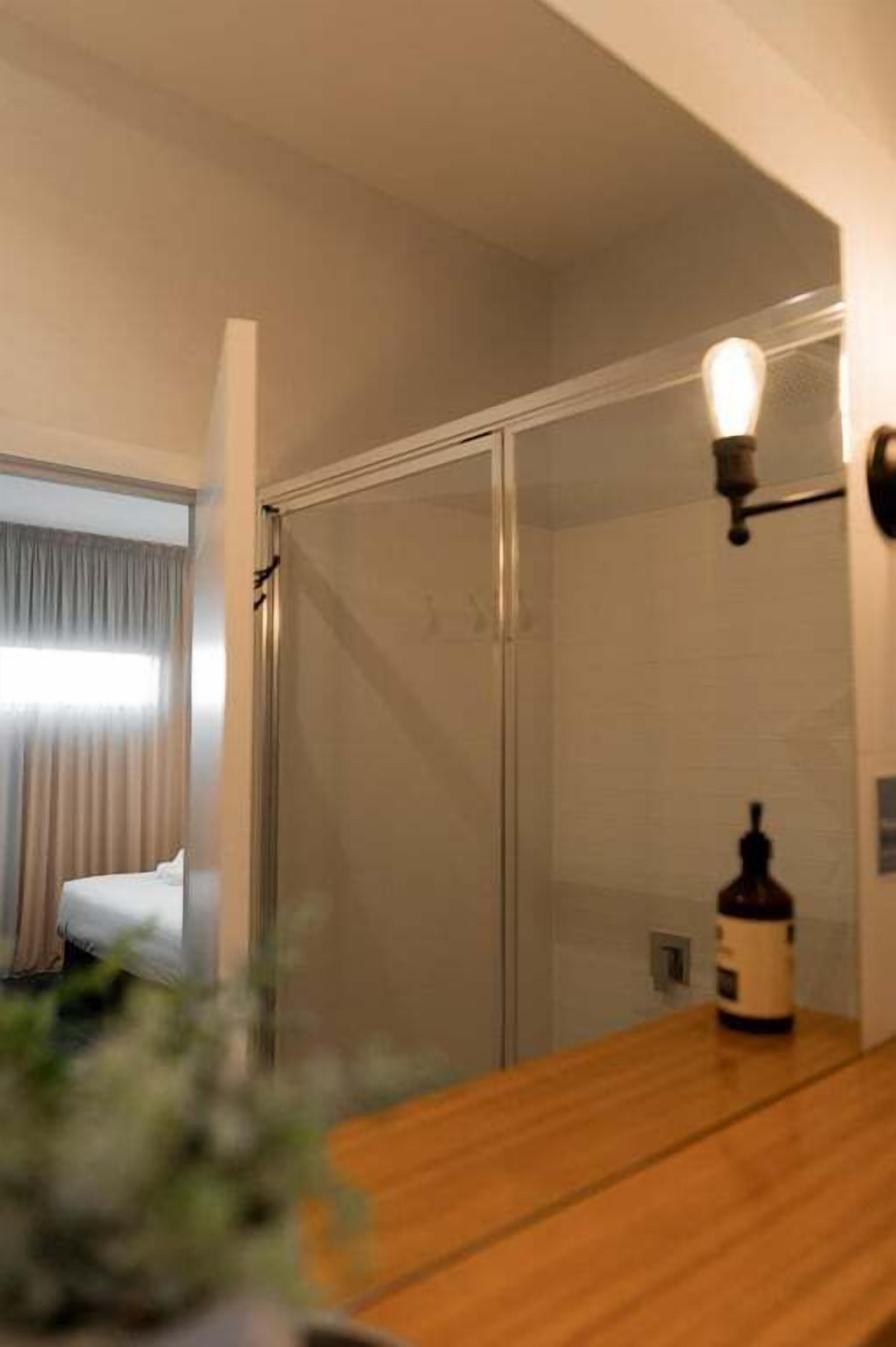 A hotel room with a bed, a wooden table, a bottle, and a wall-mounted light fixture.