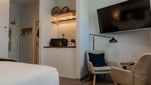 Habitación de hotel con cama, escritorio con lámpara, silla, televisión montada en la pared y estante con cestas.