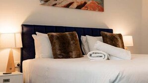 Habitación de hotel con cama, dos lámparas de noche, una mesita de noche, aire acondicionado de pared y un cuadro con una escena costera.
