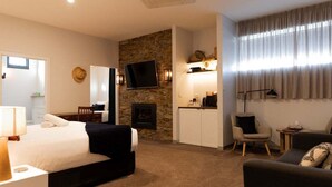 A hotel room with a bed, a TV, a fireplace, a desk, a chair, and a sofa. - Bay of Fires Holiday Suites ~ Suite 9 (Break O'Day)