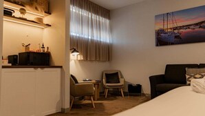 A hotel room with a bed, a desk, two chairs, a lamp, and a painting of a marina. - Bay of Fires Holiday Suites ~ Suite 9 (Break O'Day)