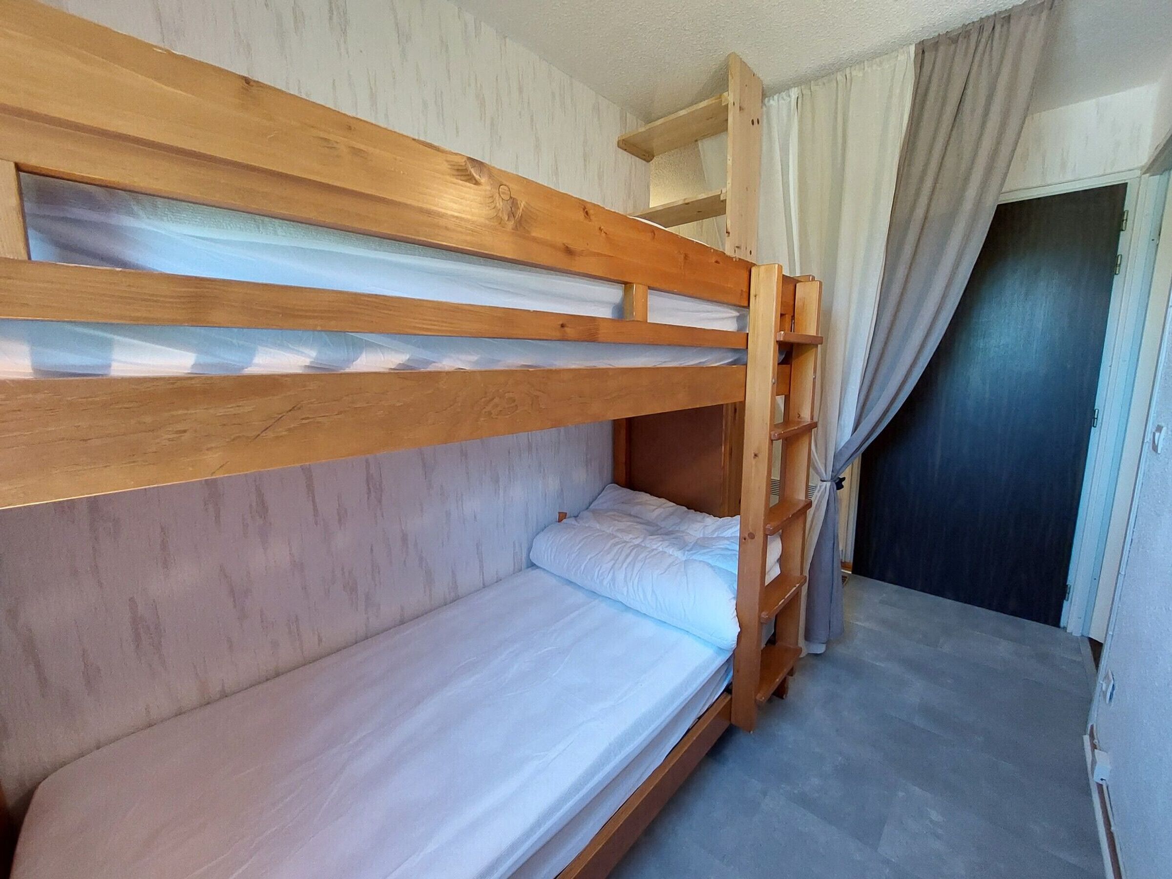 Una camera con un letto a castello, una testiera in legno, un piccolo ripiano e una tenda.