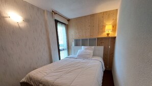 A bedroom with a bed, a window with curtains, a wall-mounted lamp, and a wooden panel wall. - Cozy 3* apartment for 6, near slopes, with parking (Autrans-Méaudre en Vercors-Autrans)