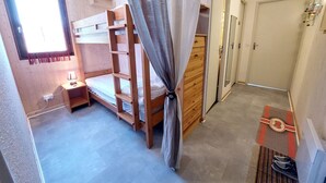 A compact bedroom with a bunk bed, a bedside table with a lamp, a wardrobe, and a door leading to another room. - Cozy 3* apartment for 6, near slopes, with parking (Autrans-Méaudre en Vercors-Autrans)