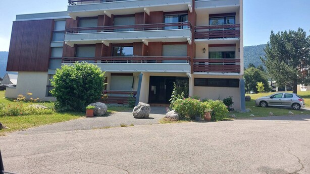 A multi-story building with balconies, a parking area, and surrounding greenery. - Cozy 3* apartment for 6, near slopes, with parking (Autrans-Méaudre en Vercors-Autrans)