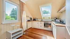 Une cuisine moderne avec un plancher en bois, des meubles blancs et une grande fenêtre offrant une vue sur la verdure.
