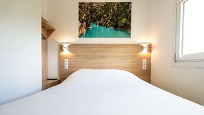 Un dormitorio con cabecera de madera, cama con ropa de cama blanca y un cuadro colgado en la pared de un lago turquesa.