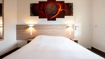Habitación de hotel con una cama grande, dos lámparas de noche, un cabecero de madera y una obra de arte colgada en la pared.