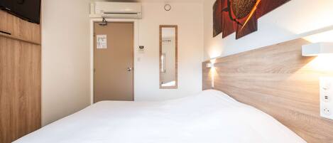 Et hotelværelse med en seng, træsengkag, et billede på væggen, et spejl og en aircondition.