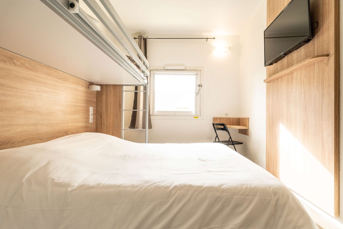 A bedroom with a bed, a TV mounted on the wall, a window, and a chair.