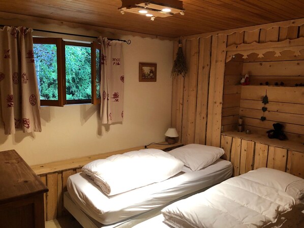 Une chambre confortable avec deux lits, une tête de lit en bois, une petite table avec une lampe et une fenêtre avec des rideaux.