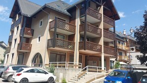 Un immeuble à plusieurs étages doté de balcons, d’un escalier et de voitures garées.